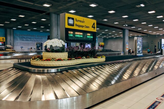 Bandă de bagaje goală într-un aeroport, cu un călător care așteaptă singur valiza care nu a mai apărut