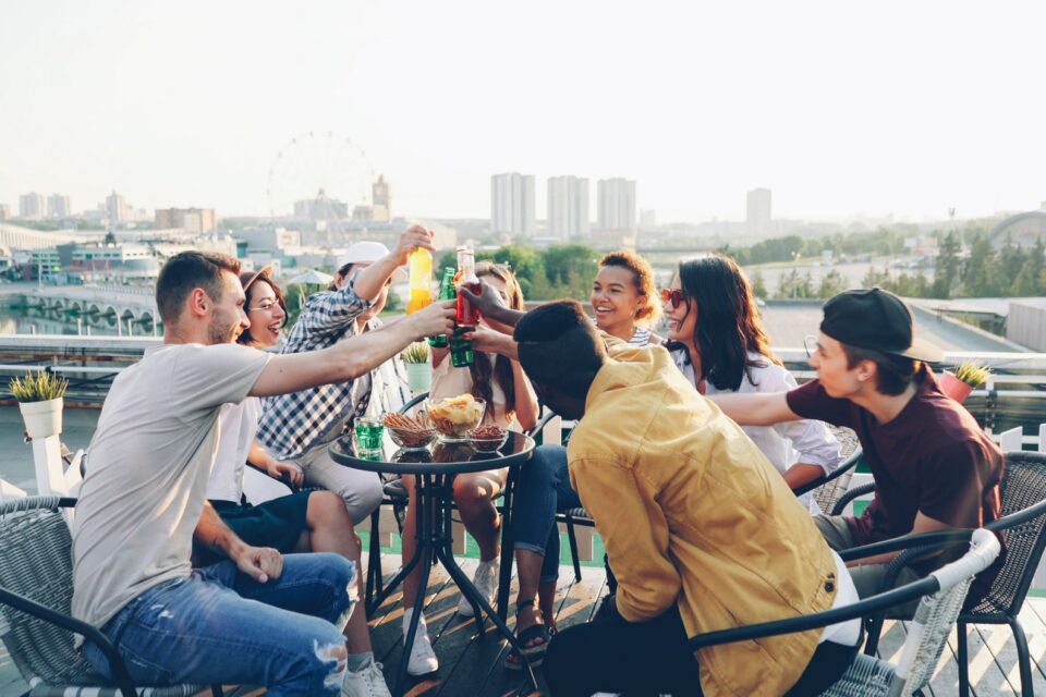 Grup de prieteni care stau la o masă pe o terasă cu vedere spre mare, la apus, în timpul unei vacanțe
